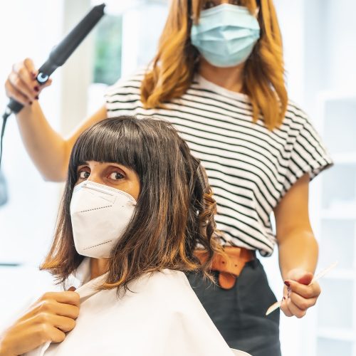 Hairdresser with mask and client, finishing the hairstyle. Reopening with security measures for hairdressers in the Covid-19 pandemic. New normal, coronavirus, social distance